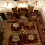 Where to Stay in Fes: Best Areas, Riads & Honest Advice (2026) Traditional riad courtyard in Fes, Morocco, seen from above with zellige tilework, carved wooden doors and sunken seating