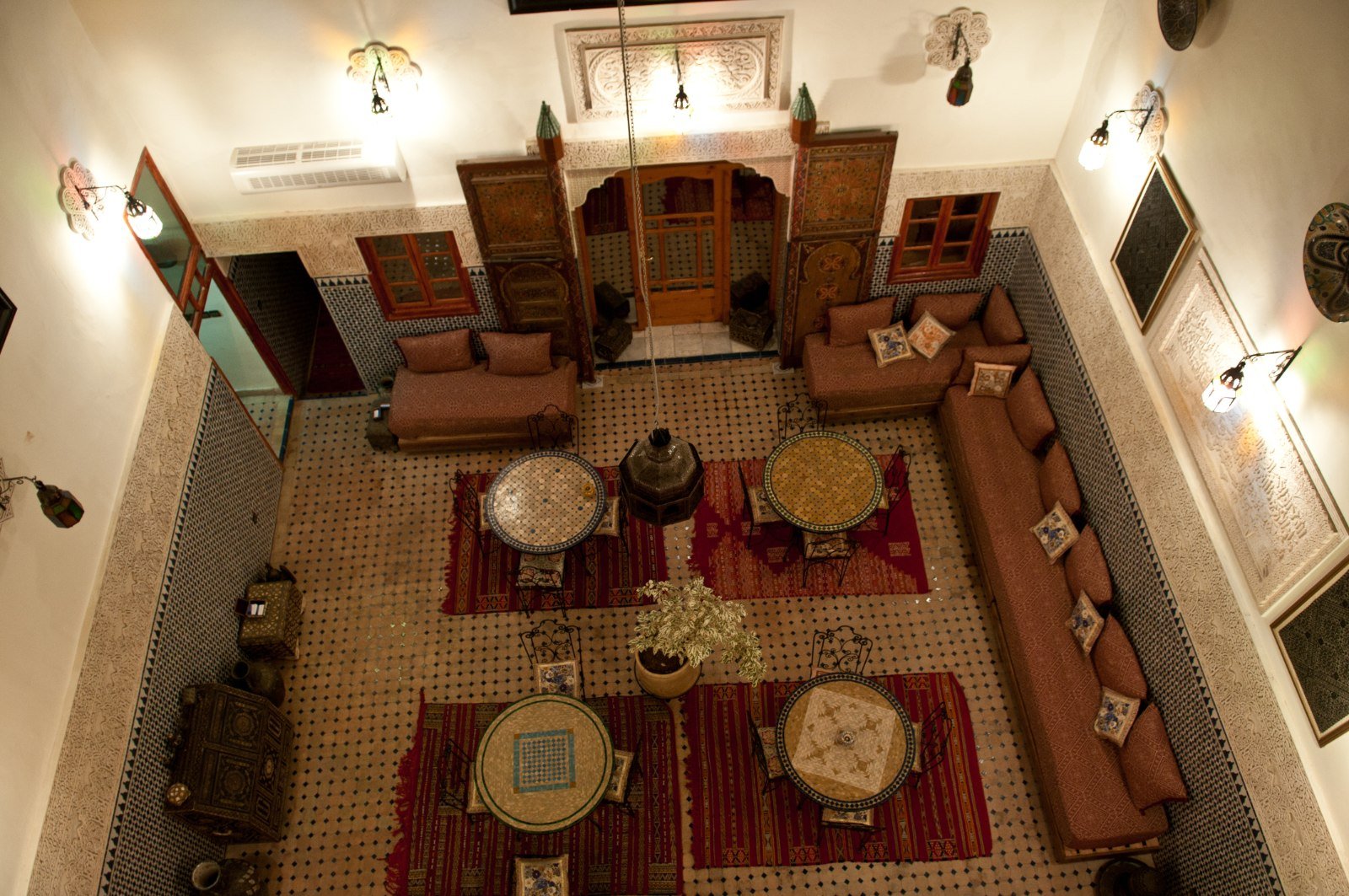 Traditional riad courtyard in Fes, Morocco, seen from above with zellige tilework, carved wooden doors and sunken seating